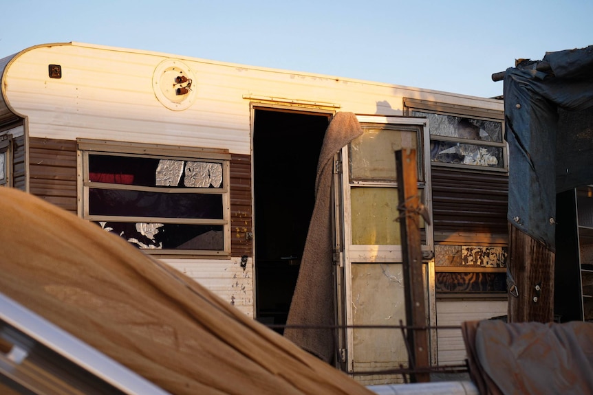 The wayward door to a wrecked caravan, with broken windows.