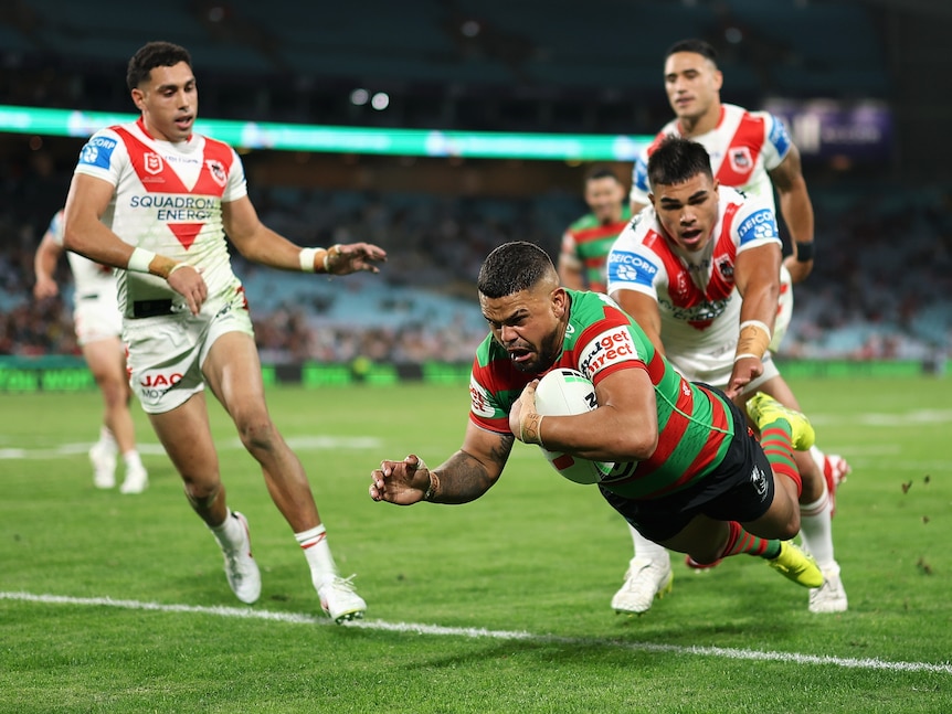 A South Sydney NRL player dives across the line to score a try as Dragons players fail to stop him.