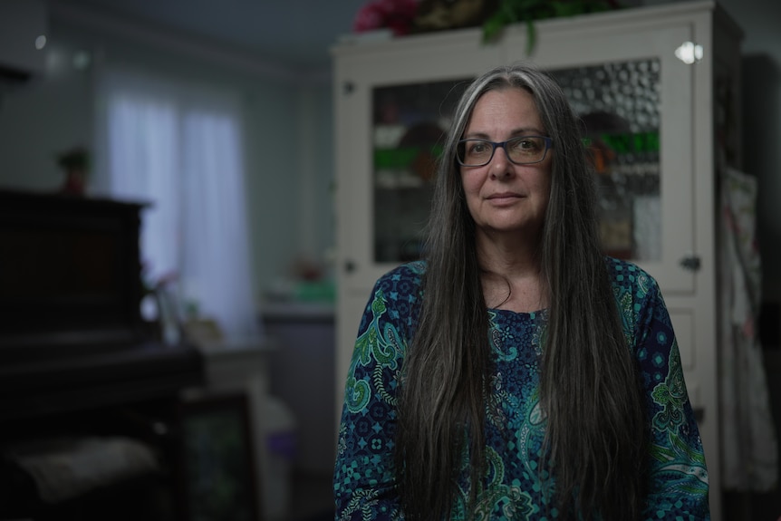 A woman with long dark hair sits in a cabin looking at the camera.