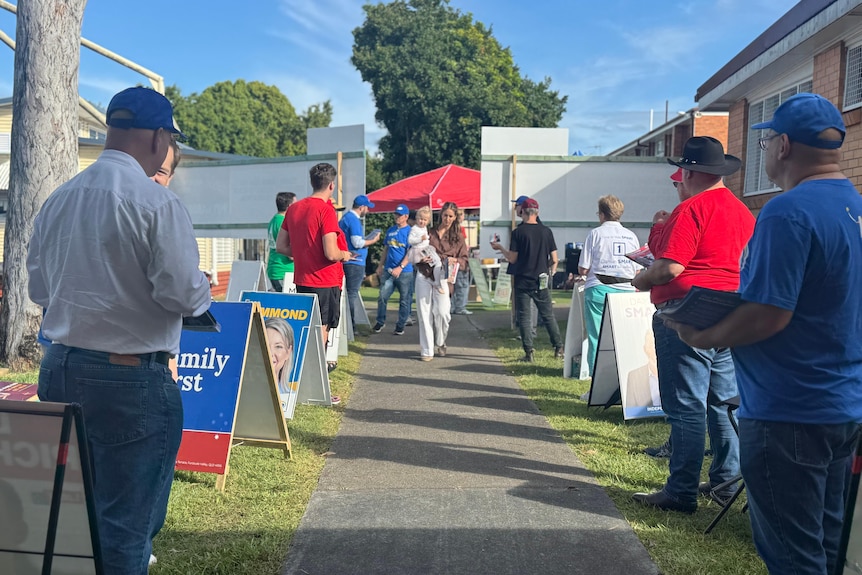 A woman holding a baby and walking along a path with election volunteers on either side.