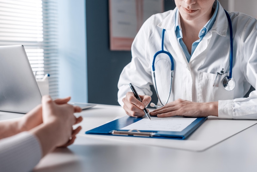 A doctor wearing a white coat and a stethoscope writes on a clipboard.
