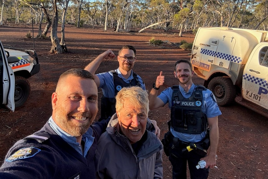 A man stands smiling with several uniformed police officers in a bush location