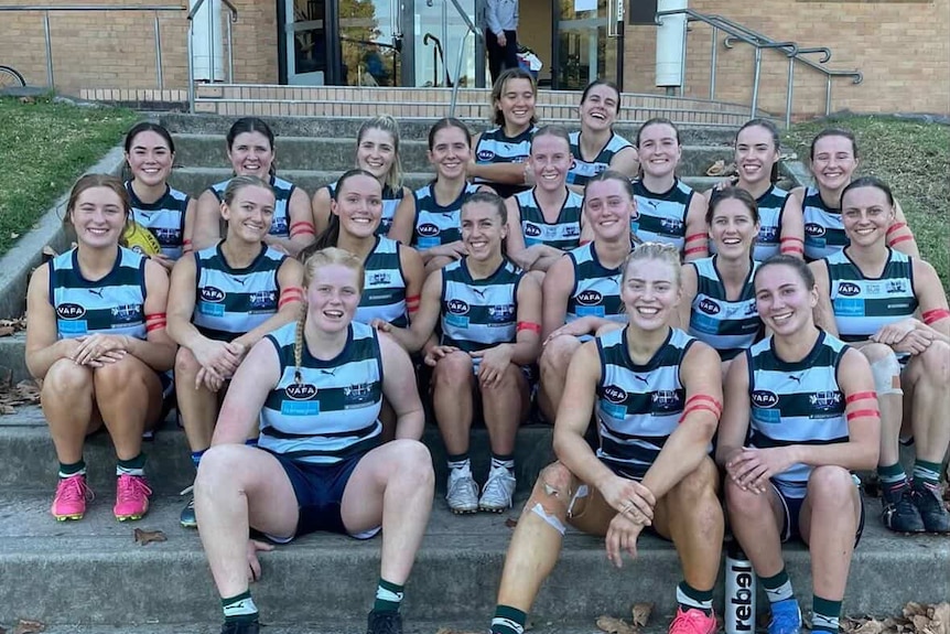 A group of women in sports uniforms, most wearing a red armband, posing on a set of steps.