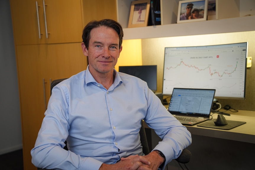 A man sitting in office with oil price chart behind him