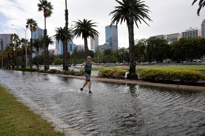 Runner Tim Mitchell makes his way out of the flooding on Riverside Drive as the Swan River breaks its banks due to the stormy weather. 