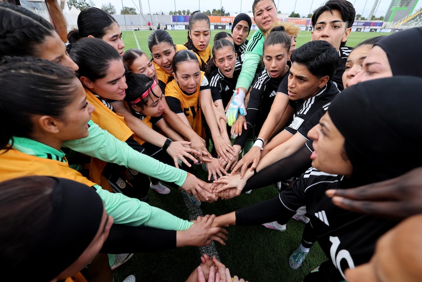 Members of the Afghan Women United football team all place their hands together in the middle of a huddle
