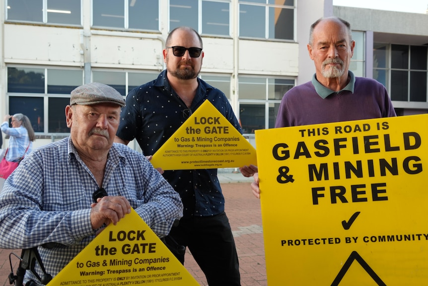 Three men holding yellow signs with anti-fracking and gas messages on them