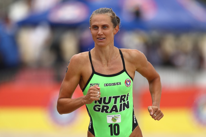 A woman in bright green swimmers runs on a beach.
