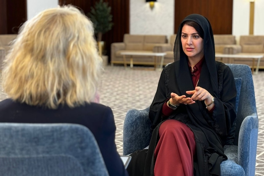 A woman sitting in a chair talking. The back of another woman's head is visible too.