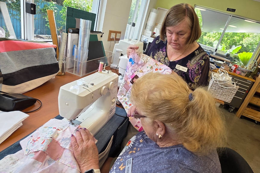 Two older ladies at a sewing machine.