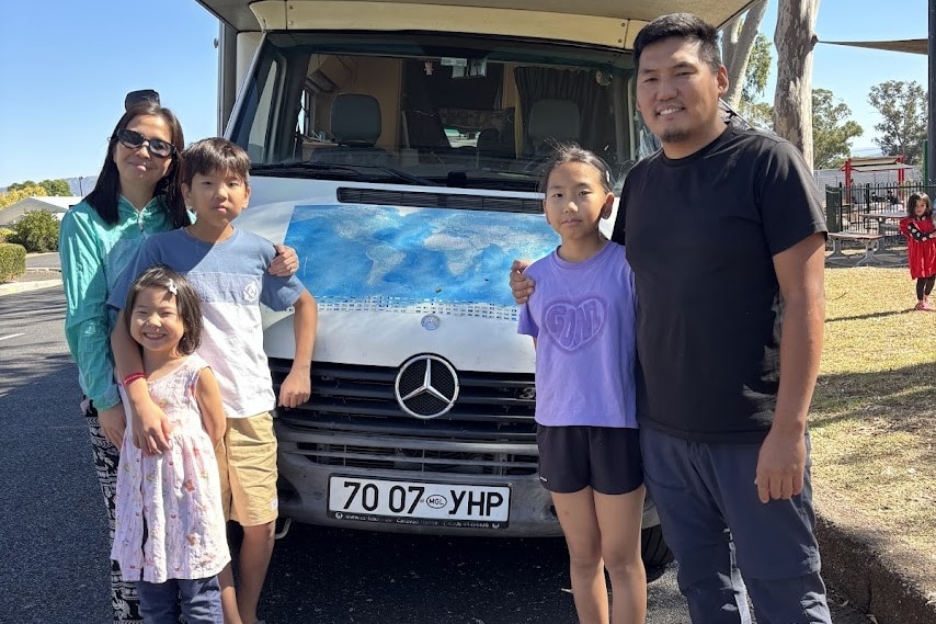 A man and woman and three kids stand in front of a van with Mongolian number plates.