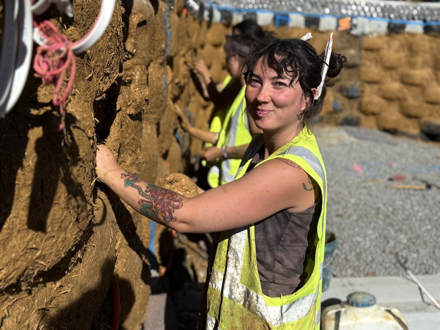 a woman smiling pushing mud into a wall