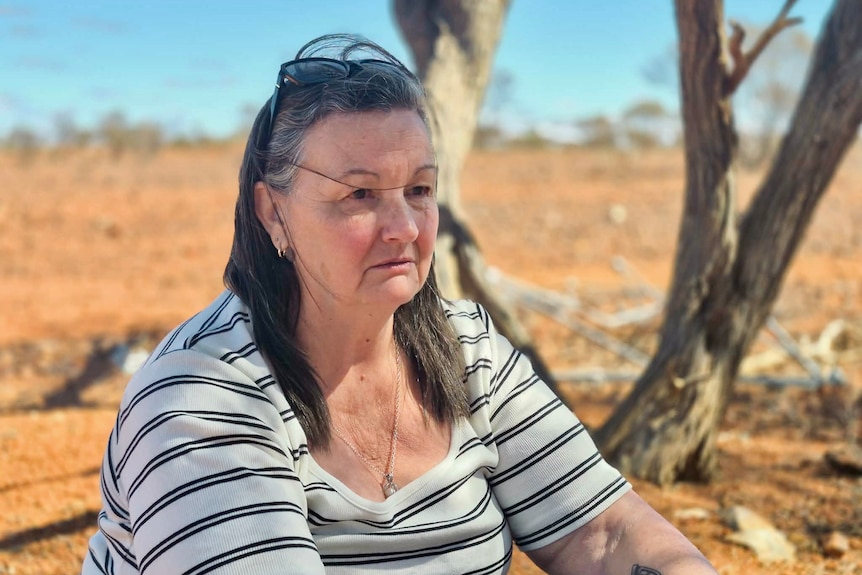 A woman sits near trees in the outback.