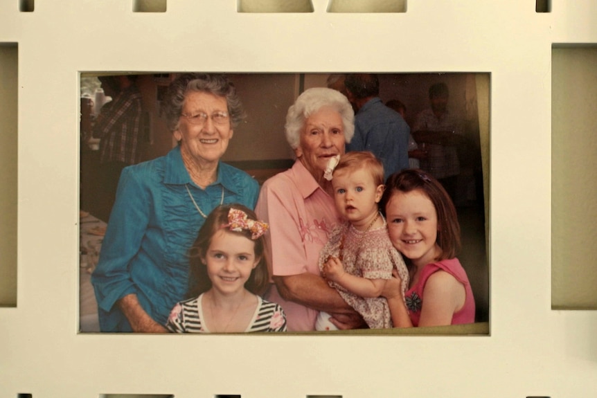 A framed photo of two older women and three young children hung on a wall.
