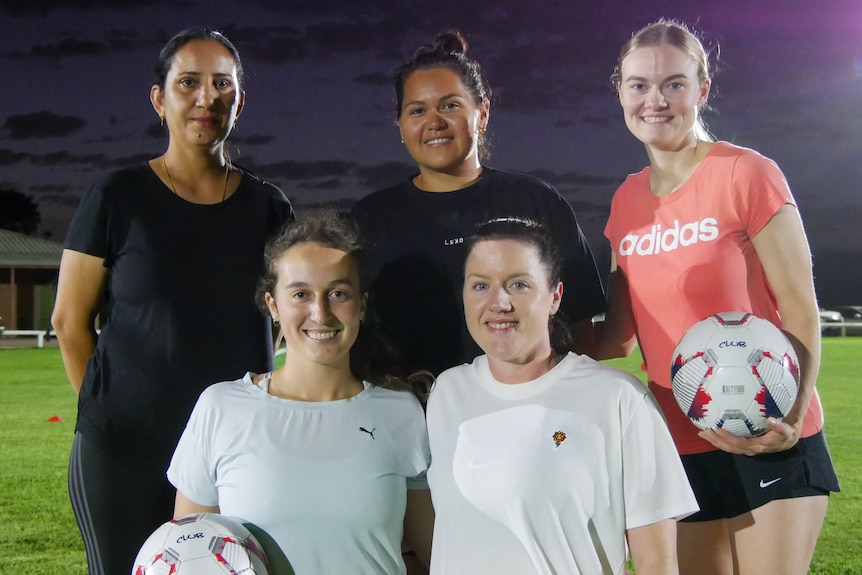 A group of women standing together, one holding a soccer ball.