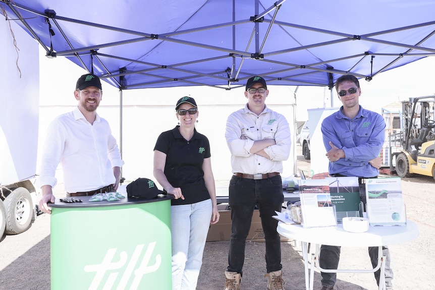Three men and a woman standing in a line at a stall at an agricultural event. 