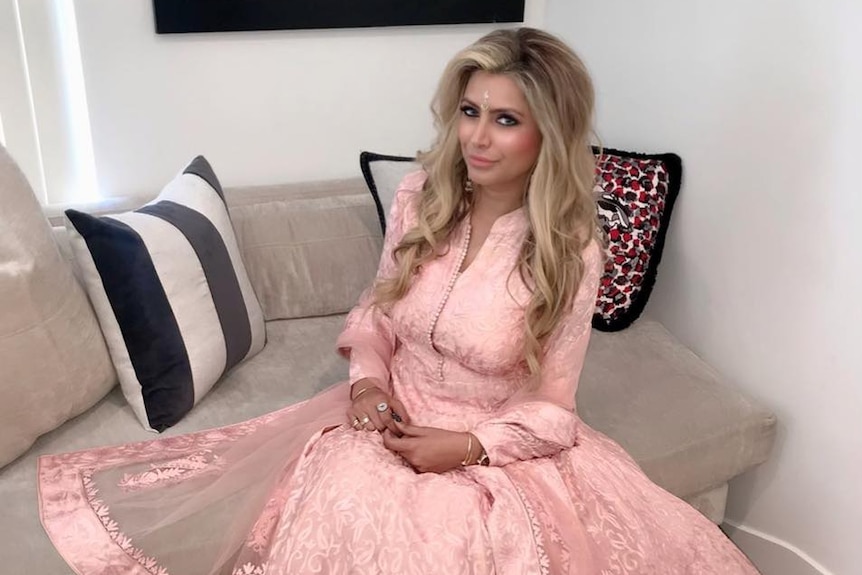 Jasveen Sangha sitting on a couch, wearing a pink dress.
