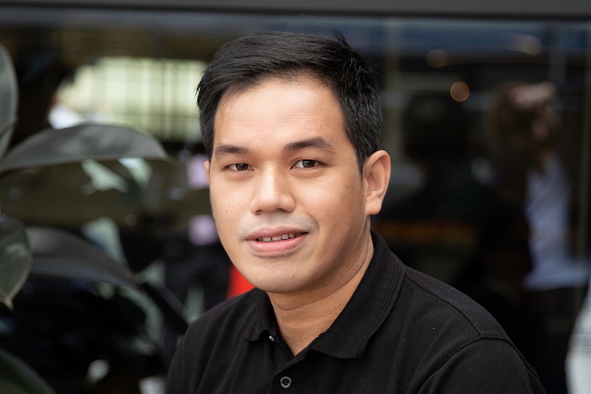 A man weaing a black polo and smiling to the camera.