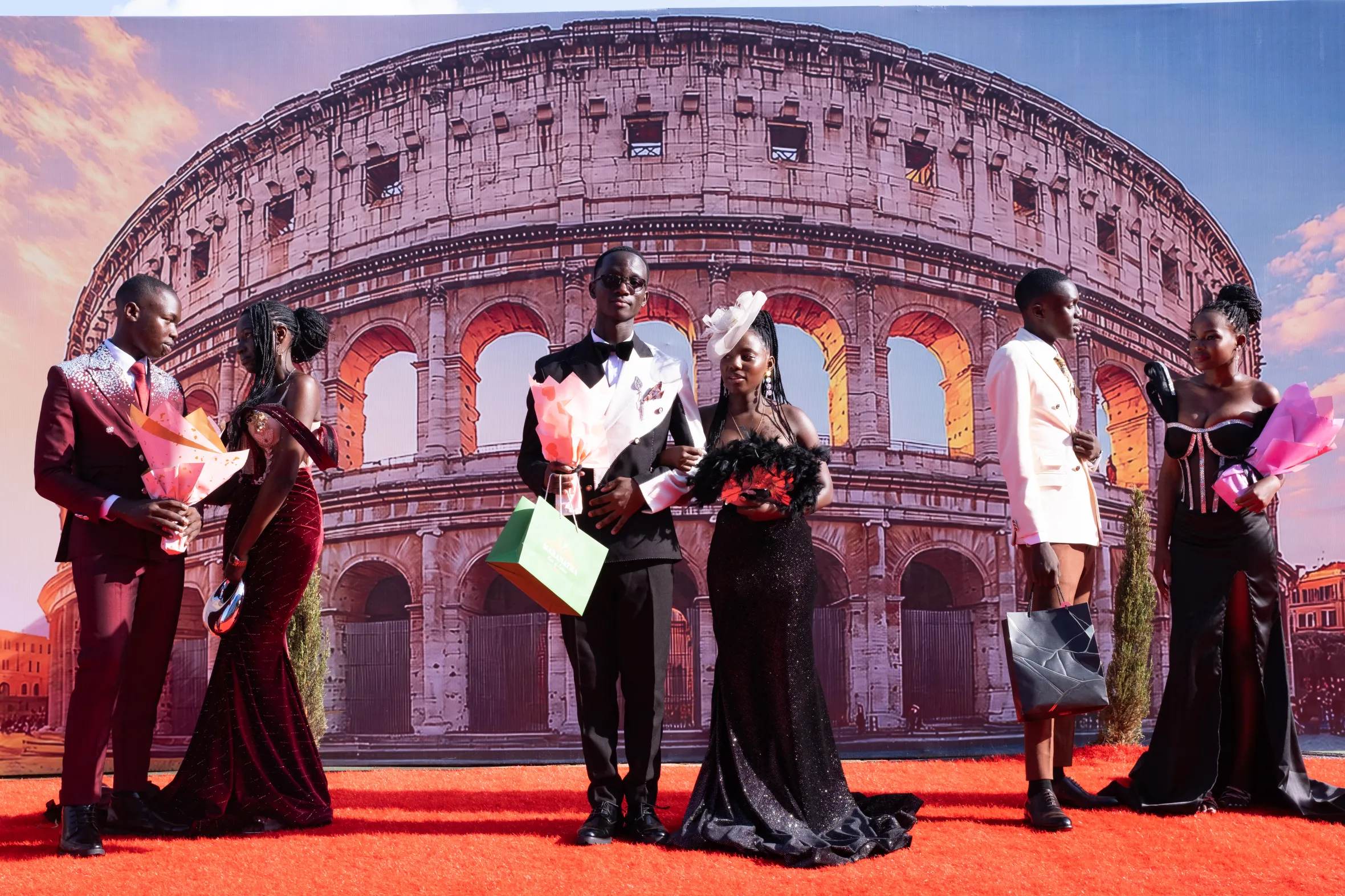 Five students in formal attire pose in front of a Colosseum backdrop at a prom.