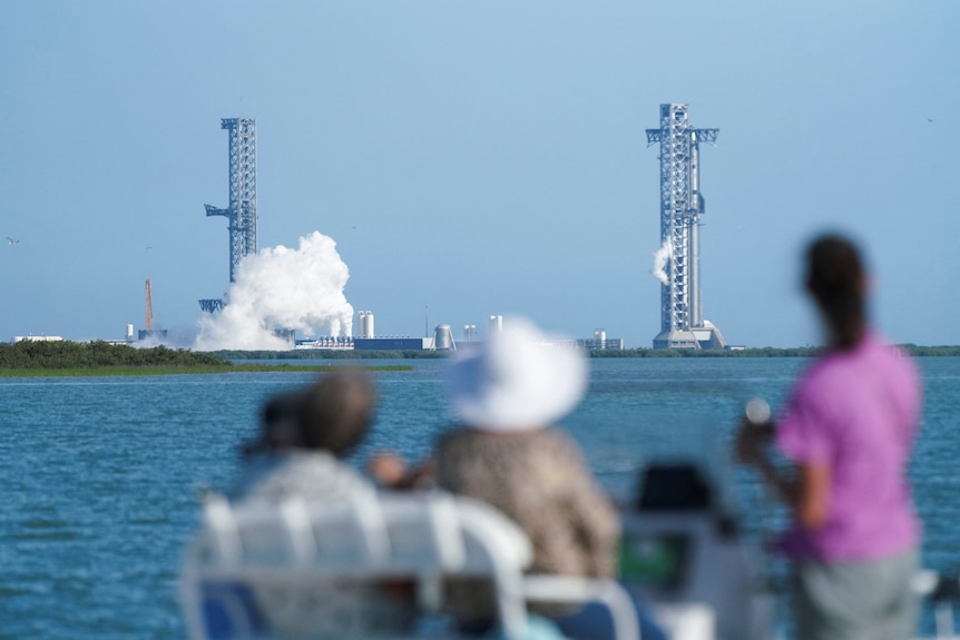 People looking over the ocean watching a rocket take off