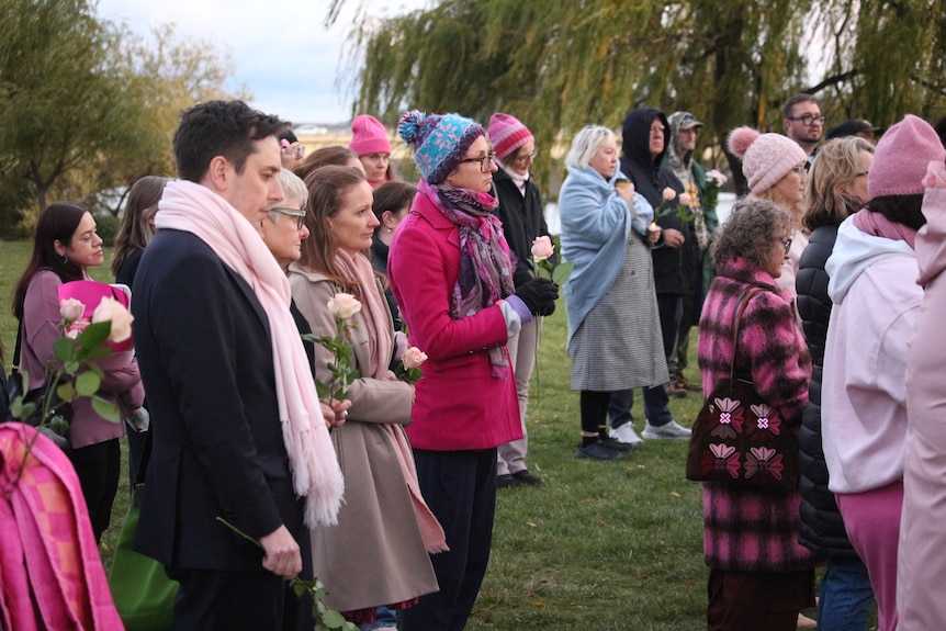 Crowd dressed in warm, pink clothing at a vigil.
