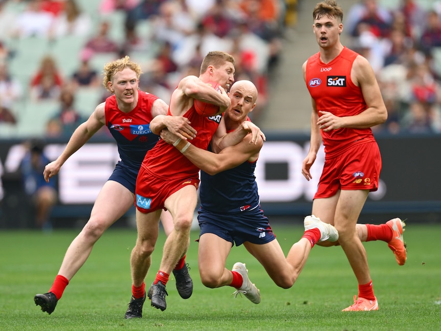 A Gold Coast Suns AFL player grimaces as he is tackled by a number of Melbourne players.