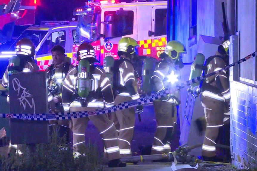 A group of firefighrers responding to a fire at night, behind police tape