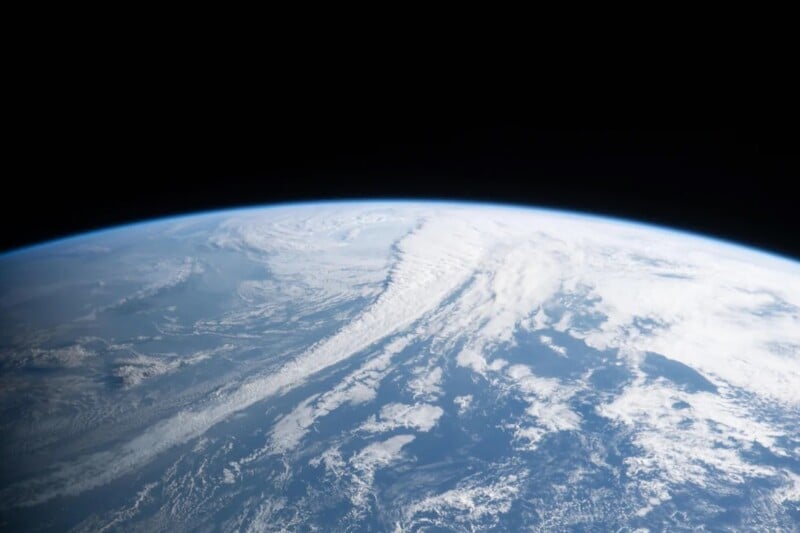 A view of Earth from space, showing its curved horizon with white clouds over blue oceans and land, beneath the blackness of outer space.
