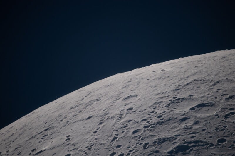 A close-up view of the moon's surface, showing numerous craters and rough terrain against a dark, black sky.