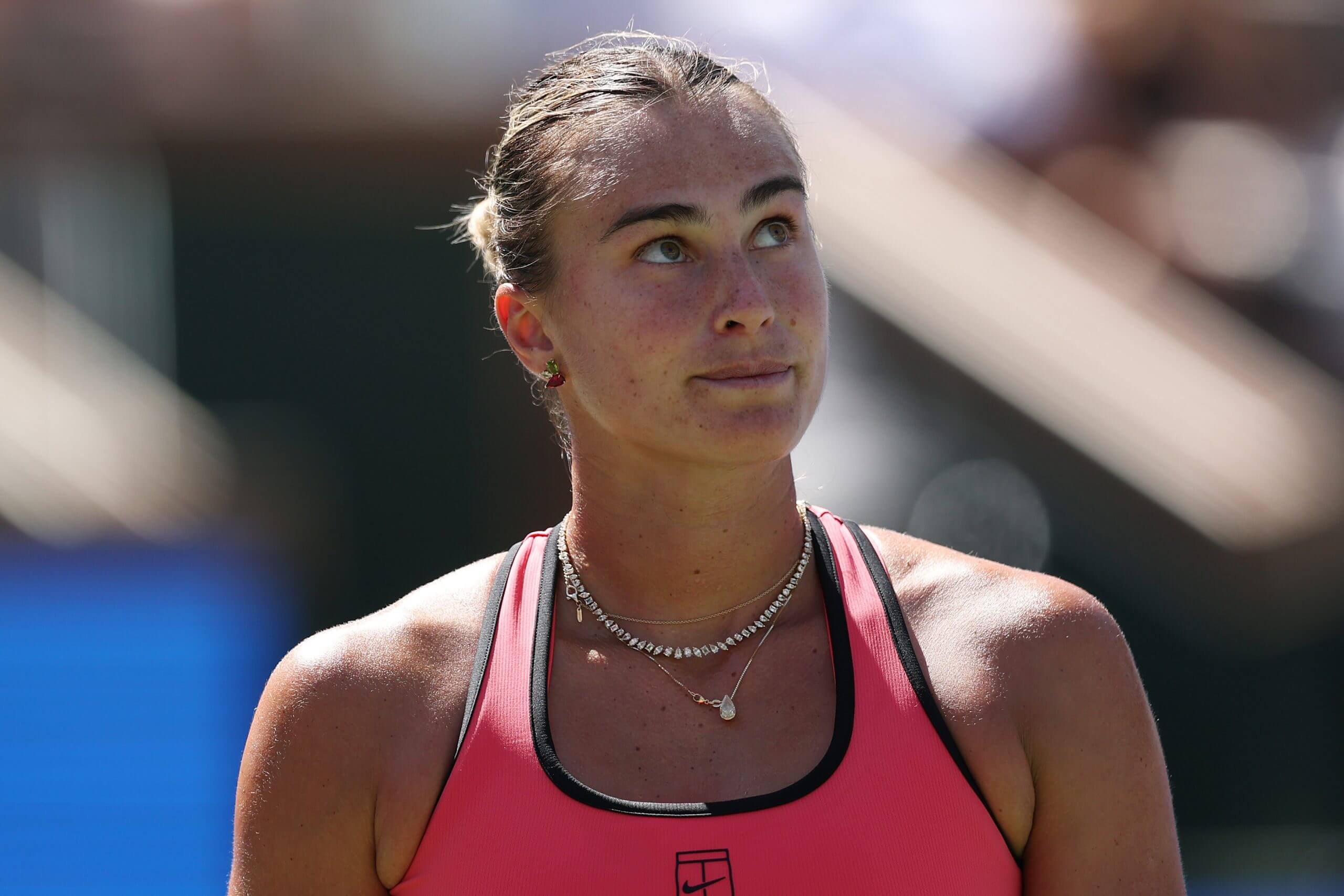 Aryna Sabalenka looks on wearing a pink tennis outfit.