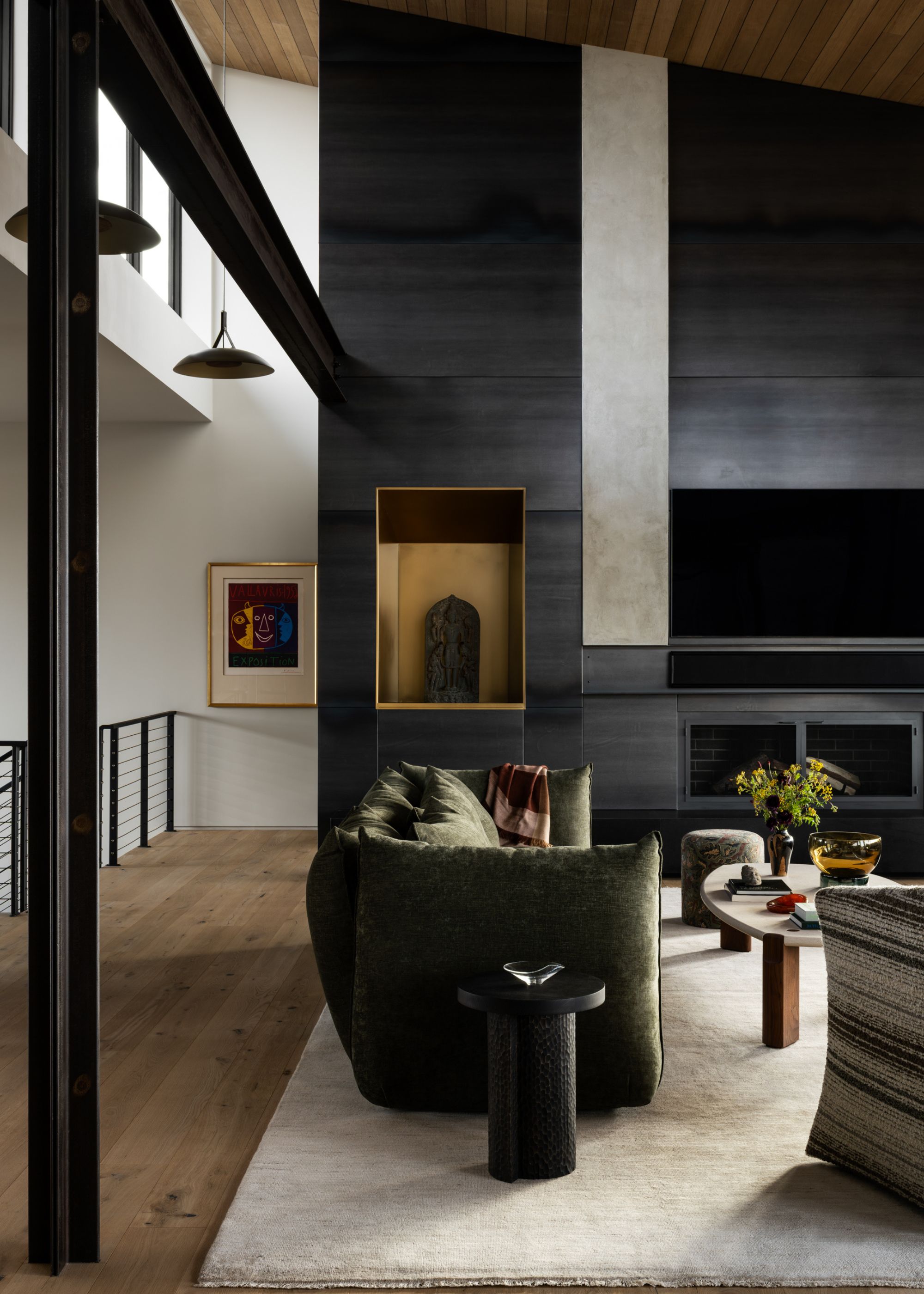 A black built-in fireplace surround with a brass niche housing a sculpture within a modern living space with a green sofa, coffee table and black side table
