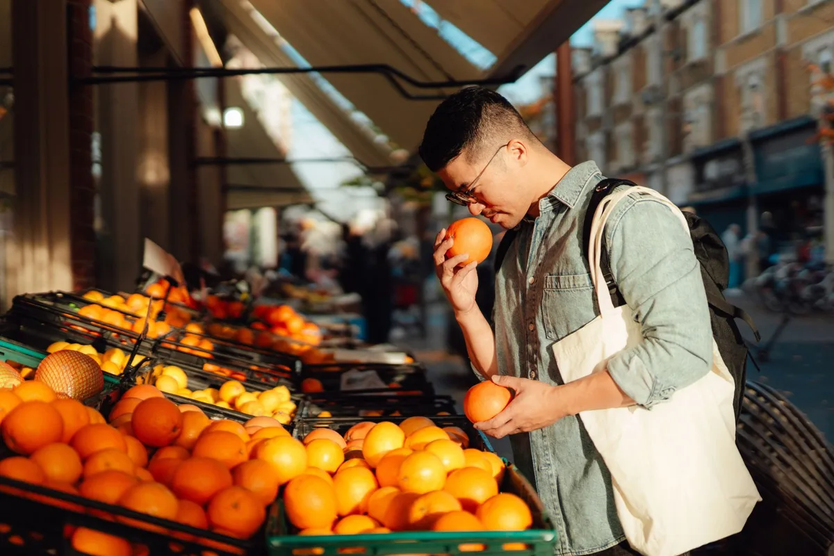 A man smells an orange at an outdoor stall