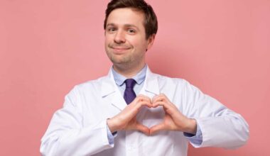 A doctor in a white coat makes a heart shape with his hands and holds it over his chest where his heart is placed.