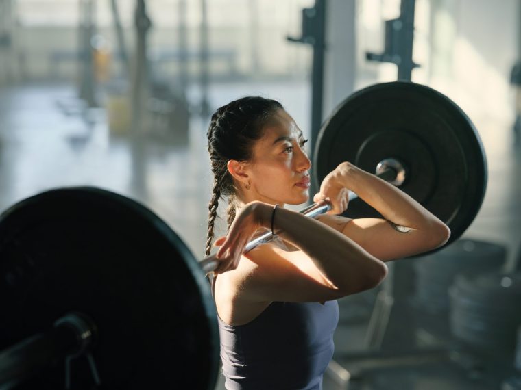 Woman lifting barbell with heavy weights in cross training gym - stock photo