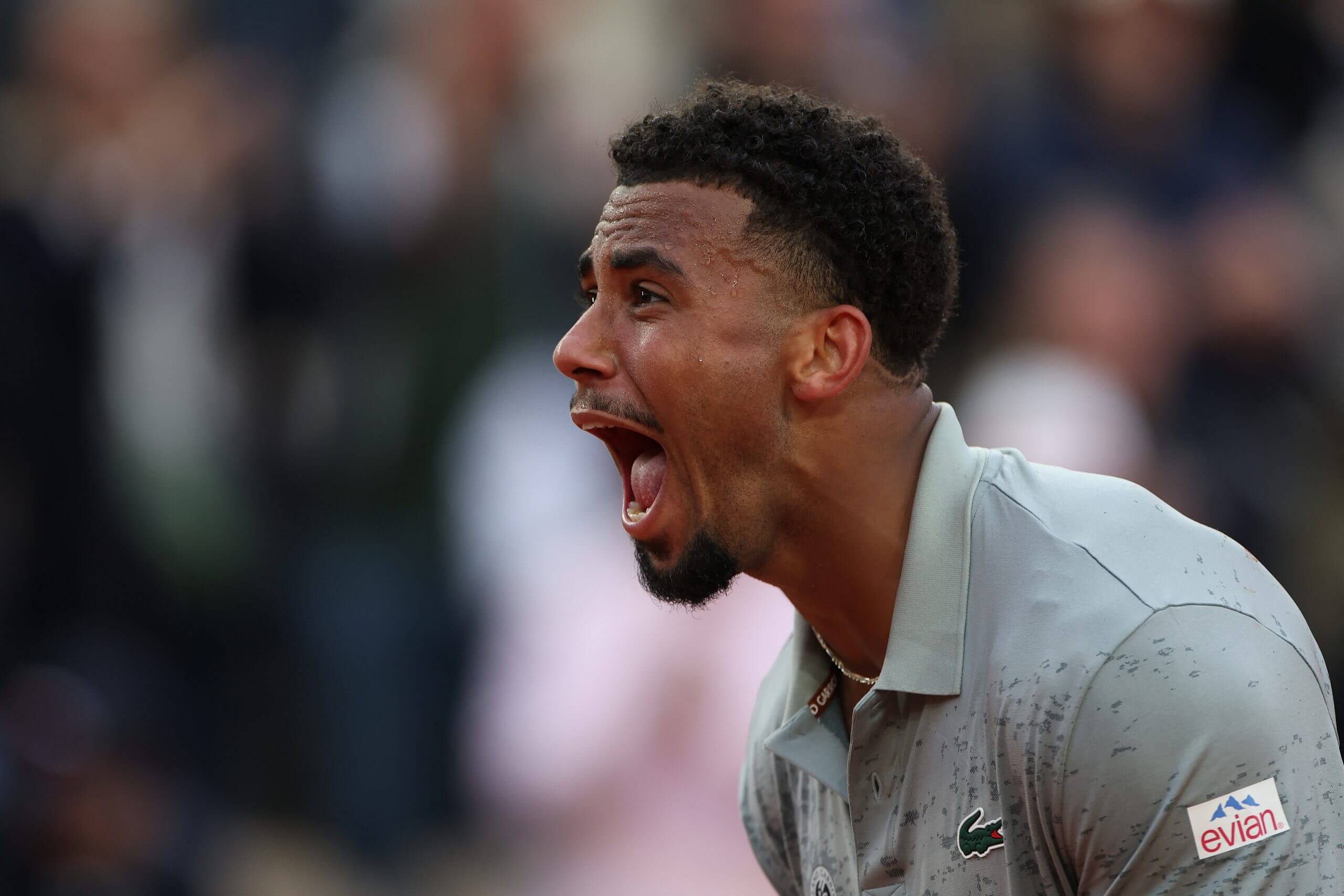 Arthur Fils roars in delight wearing a grey-green tennis outfit.