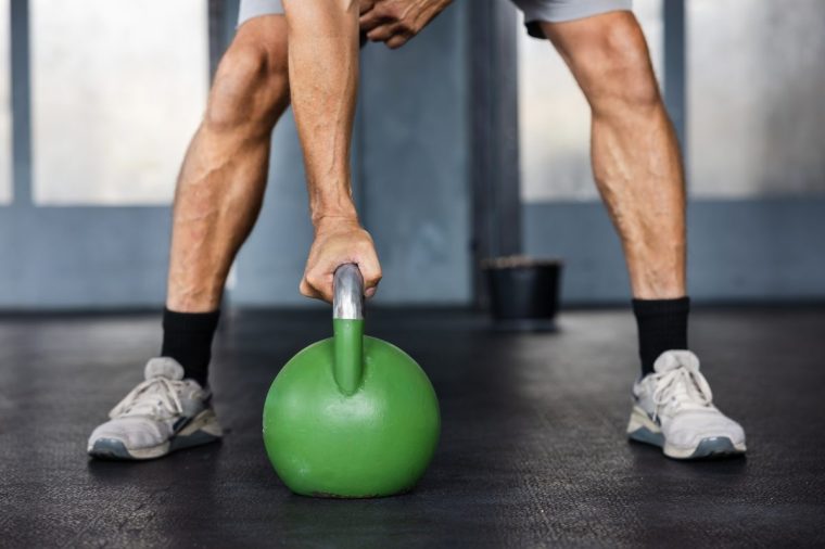 Close up of male athlete gripping heavy green kettlebell during strength training exercise in cross training gym - stock photo
