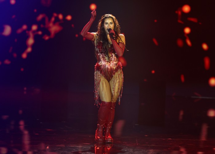 Eurovision-2026-germany Sarah Engels singing intro a microphone on stage with arm in the air above her head looking ahead.