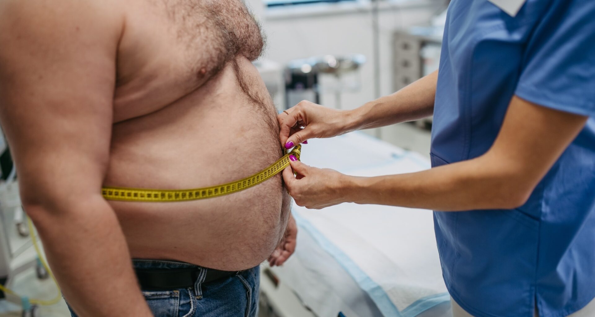 Female doctor measuring waist of overweight patient using tape measure.