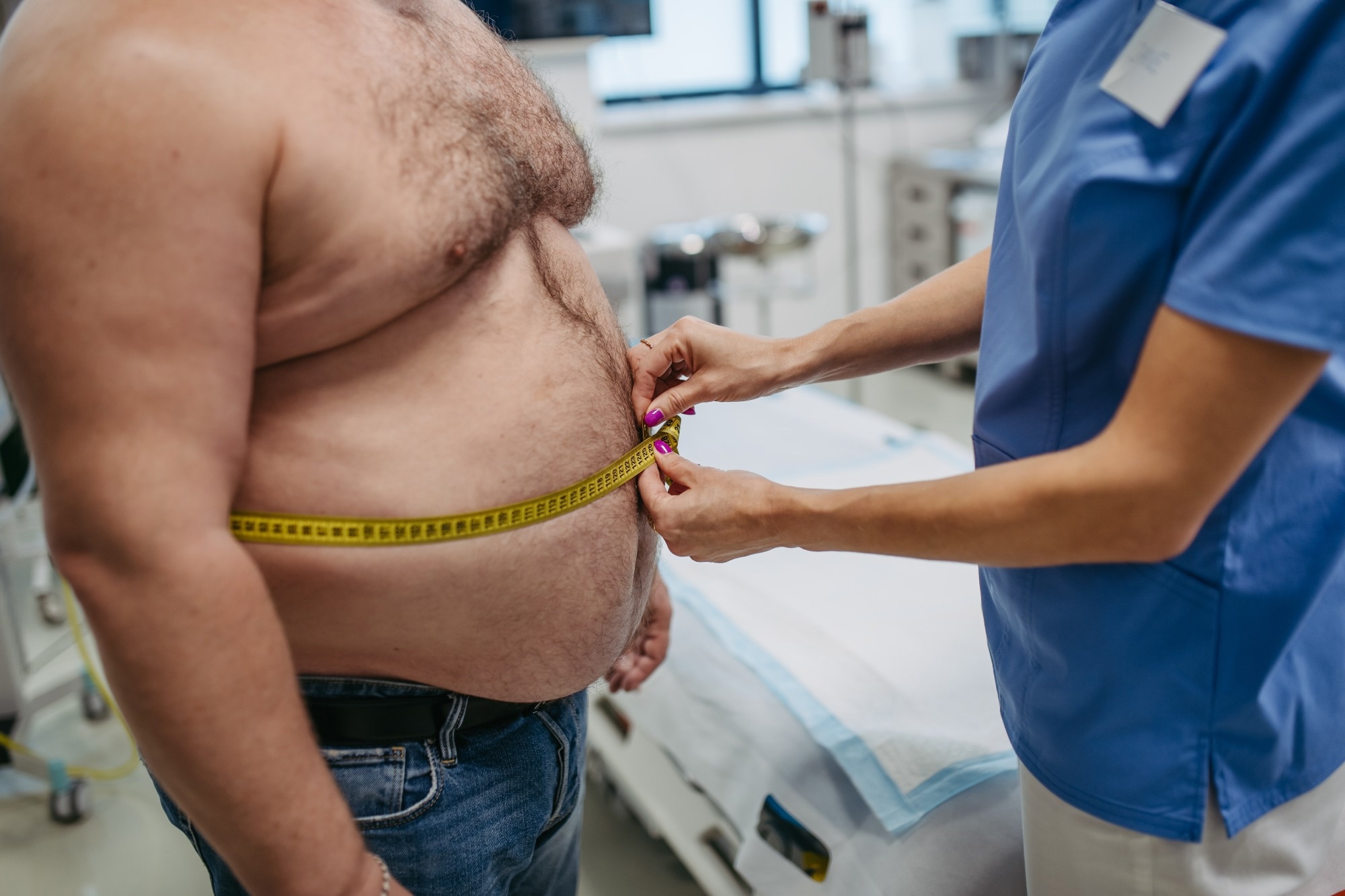 Female doctor measuring waist of overweight patient using tape measure.