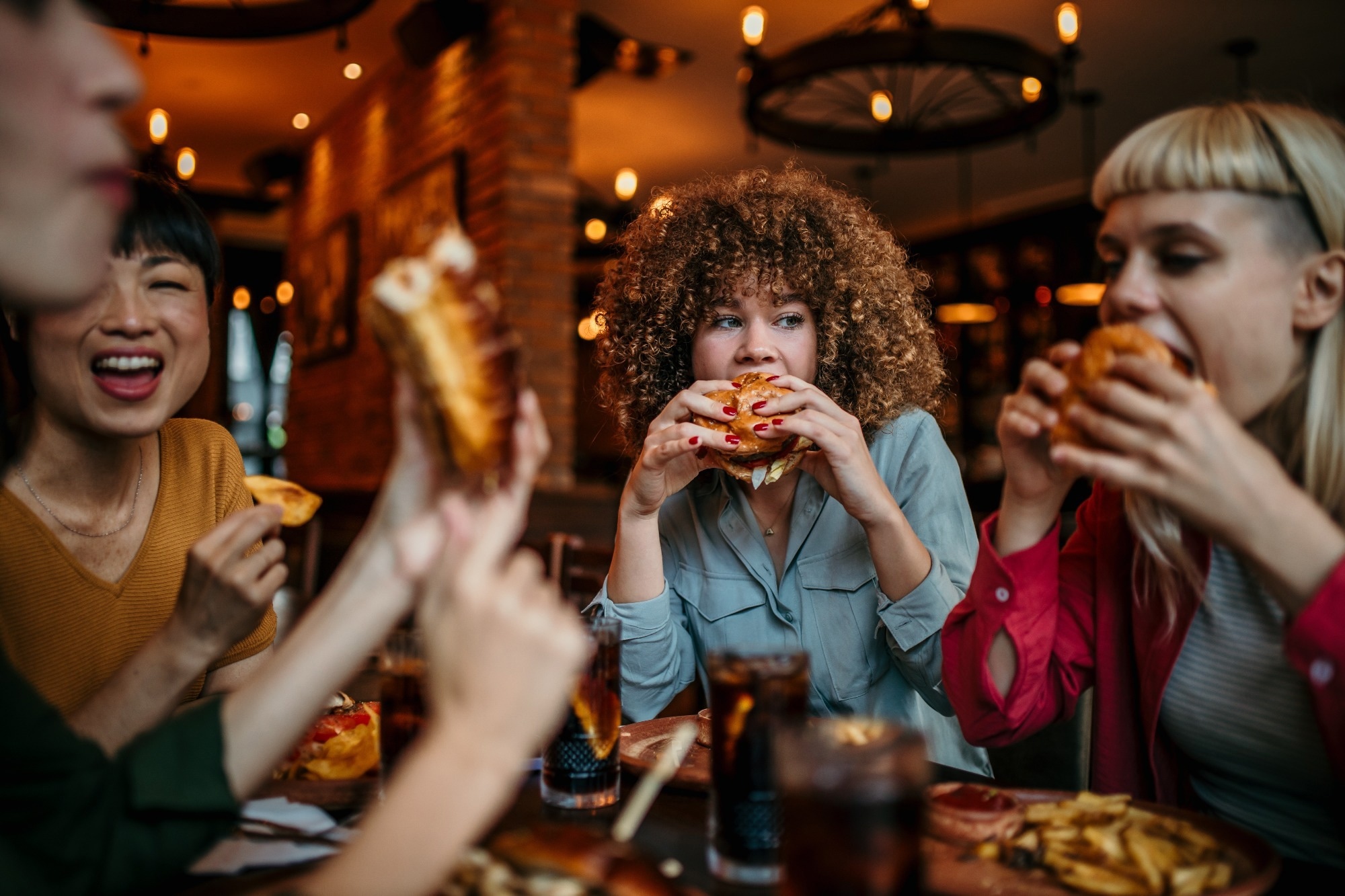Young happy women eating burgers and talking in a pub