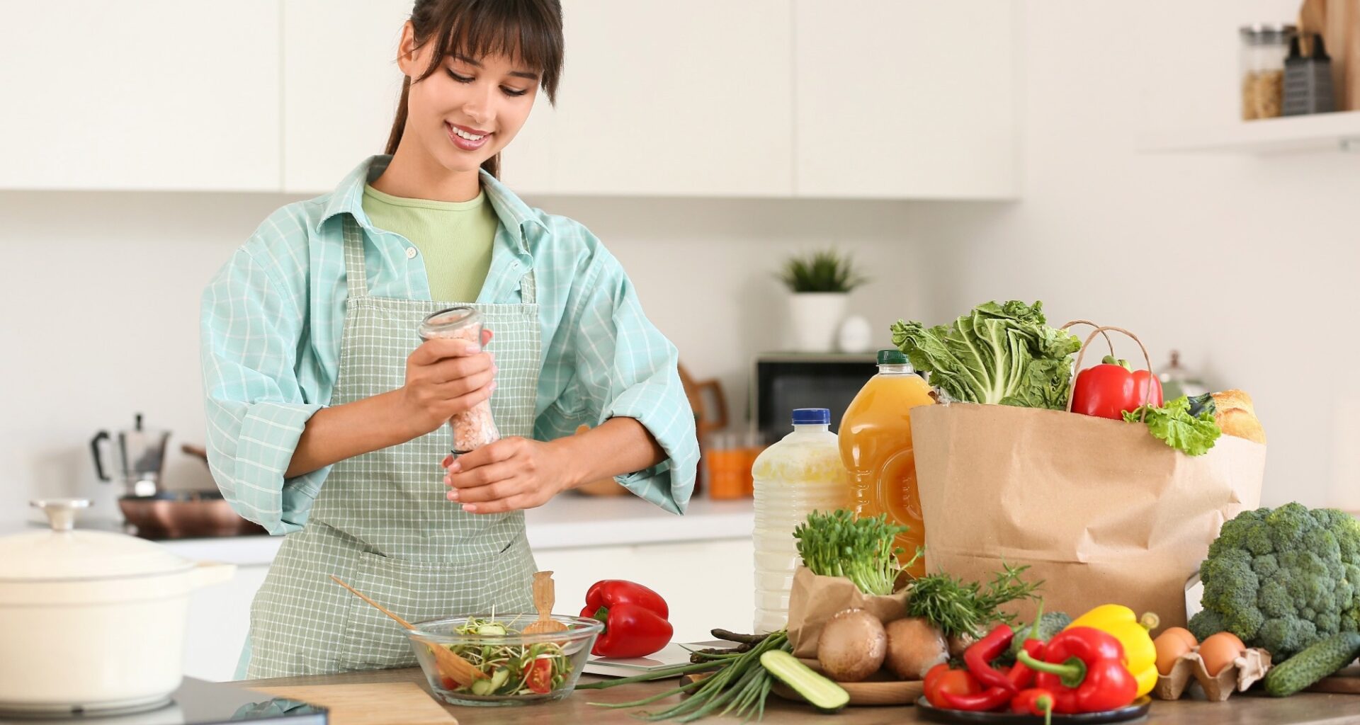 Young woman salting vegetable salad in kitchen