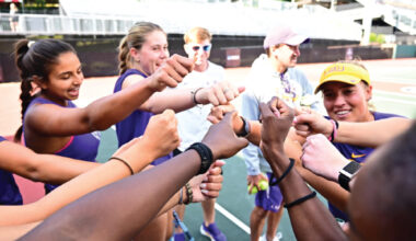 Group of diverse young athletes in a circle joining their fists for a team cheer on a track field.