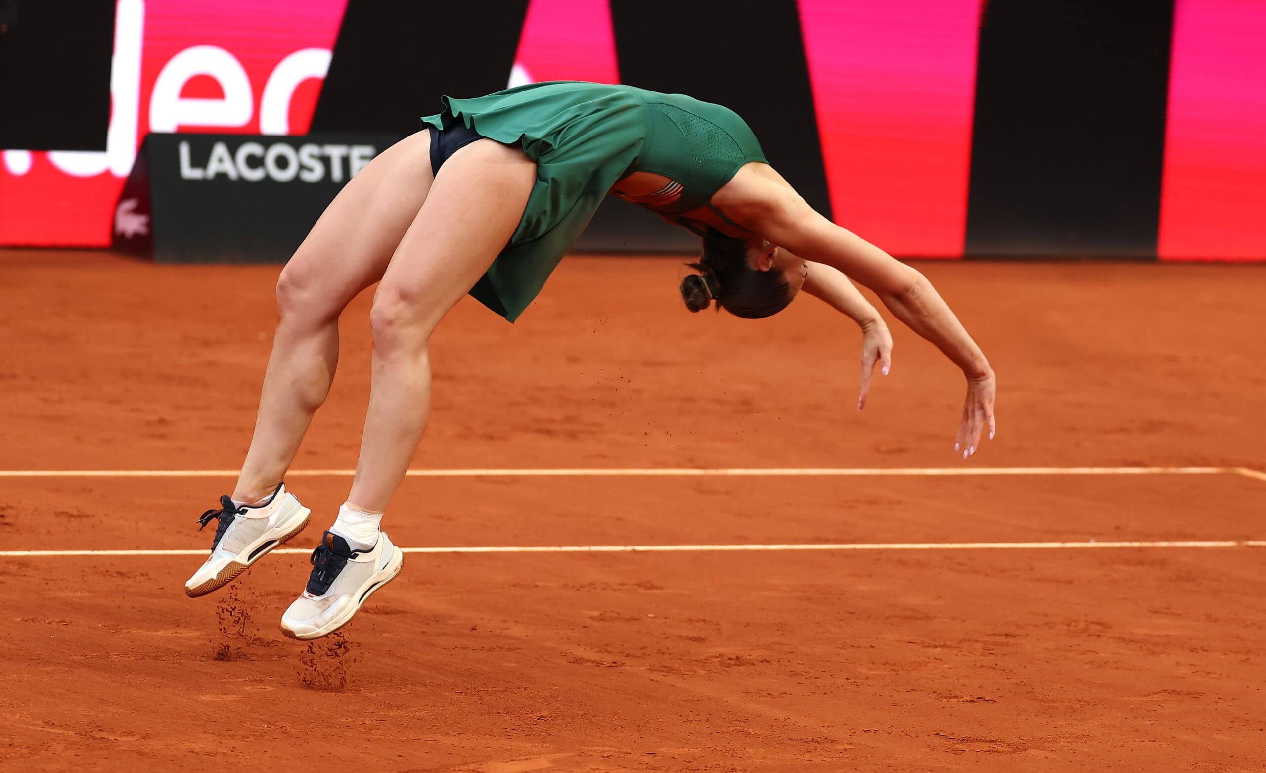 Marta Kostyuk does a backflip on a clay tennis court.