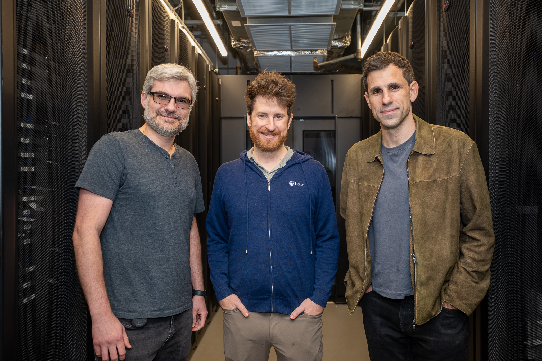 Three researchers stand side-by-side between banks of servers. 