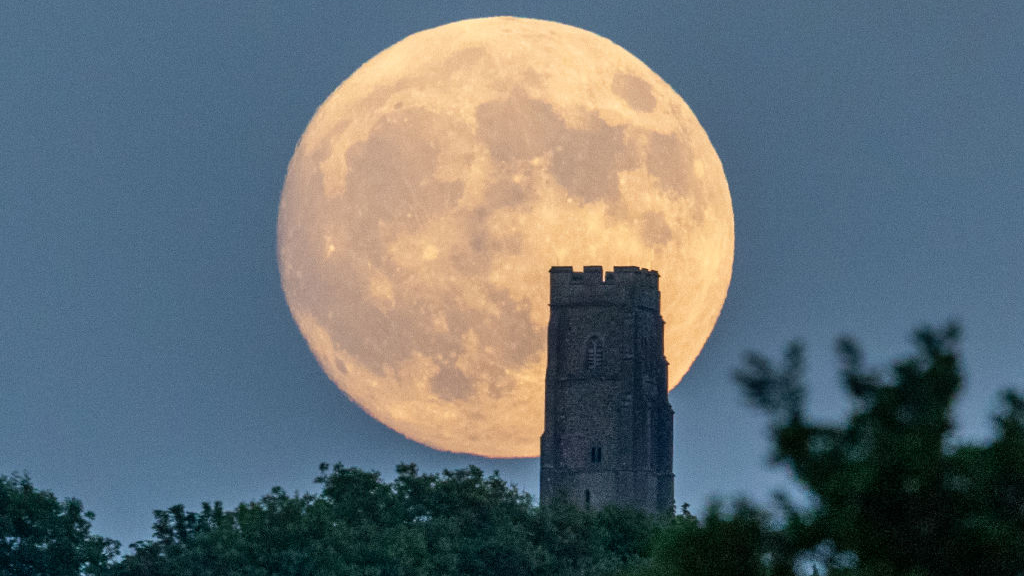 People gather as a strawberry supermoon rises behind Glastonbury Tor on June 13, 2022 in Glastonbury, England. Tonight's supermoon, so called because it is one of the closest full moons to the Earth this year, is also known as a strawberry moon. (Photo by Matt Cardy/Getty Images)