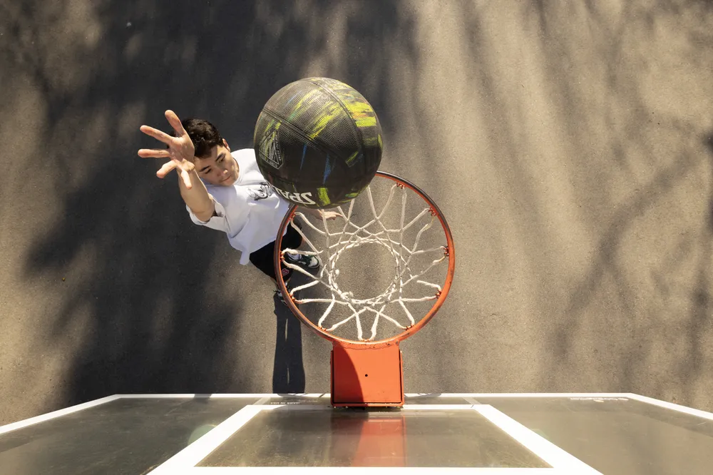 A shot from overtop of the net of Ian going for a layup.