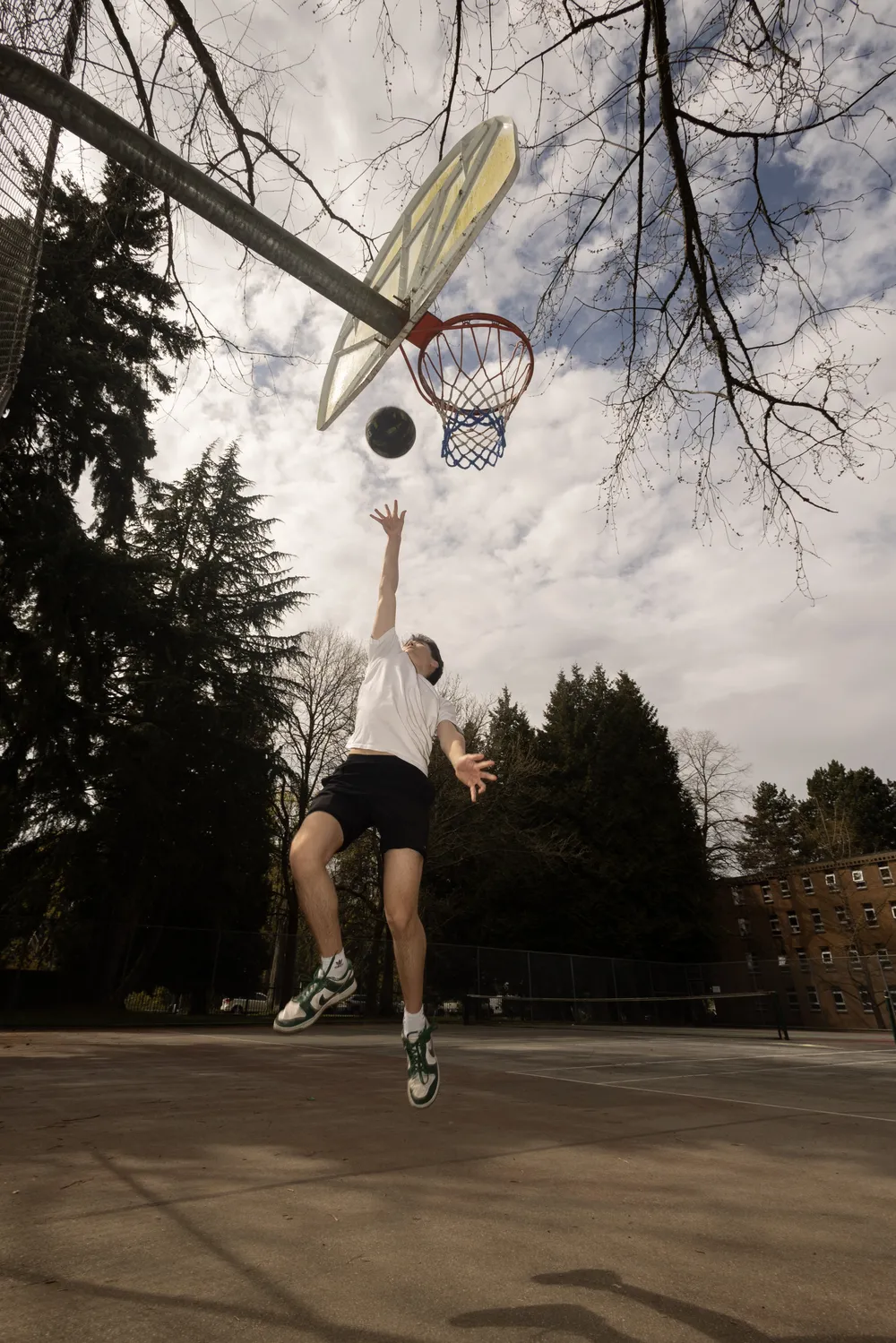Ian goes up for a layup at the Vanier courts, with pine trees in the background.