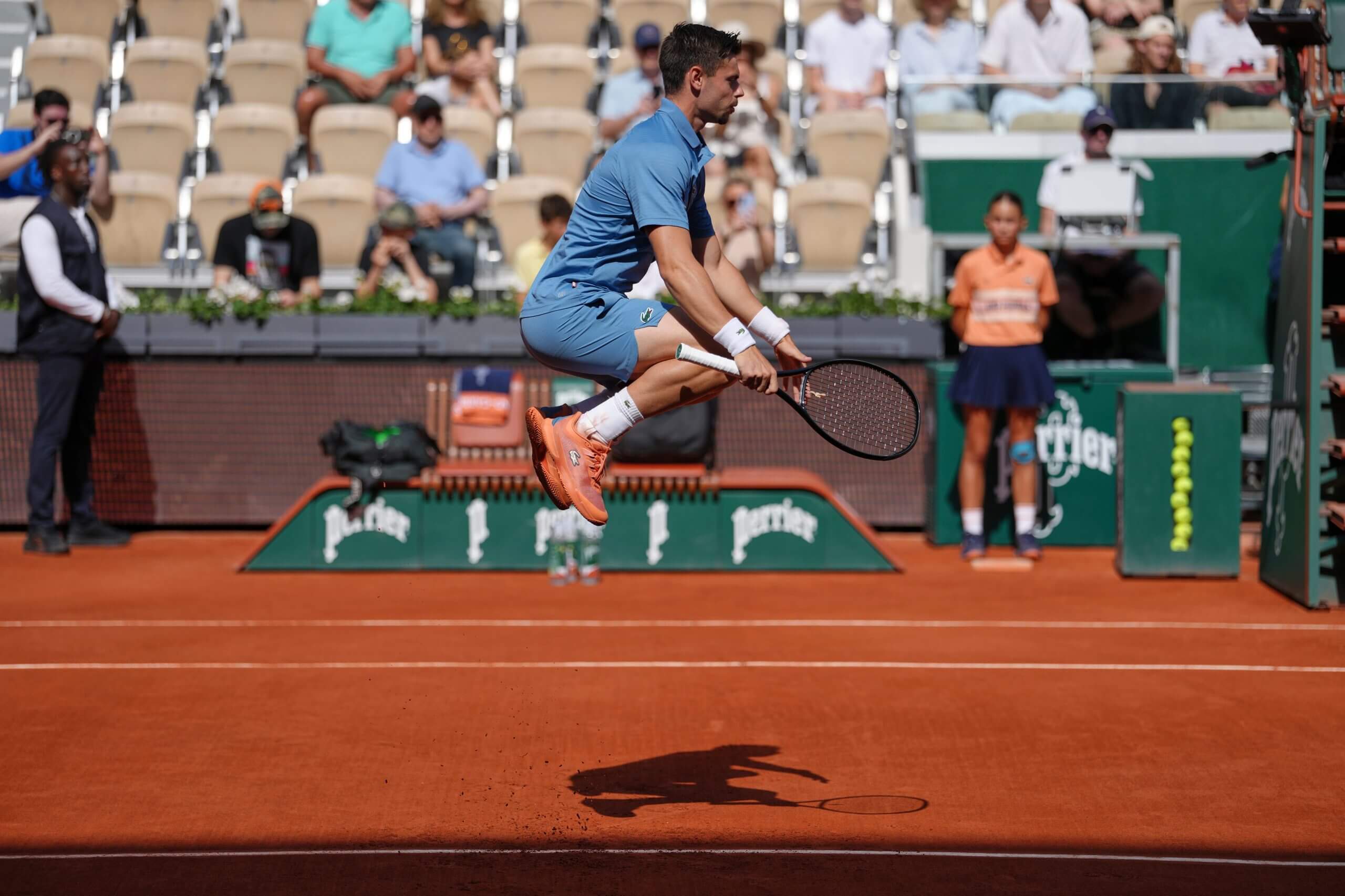 Arthur Géa leaps in the air above a clay court wearing a blue outfit.
