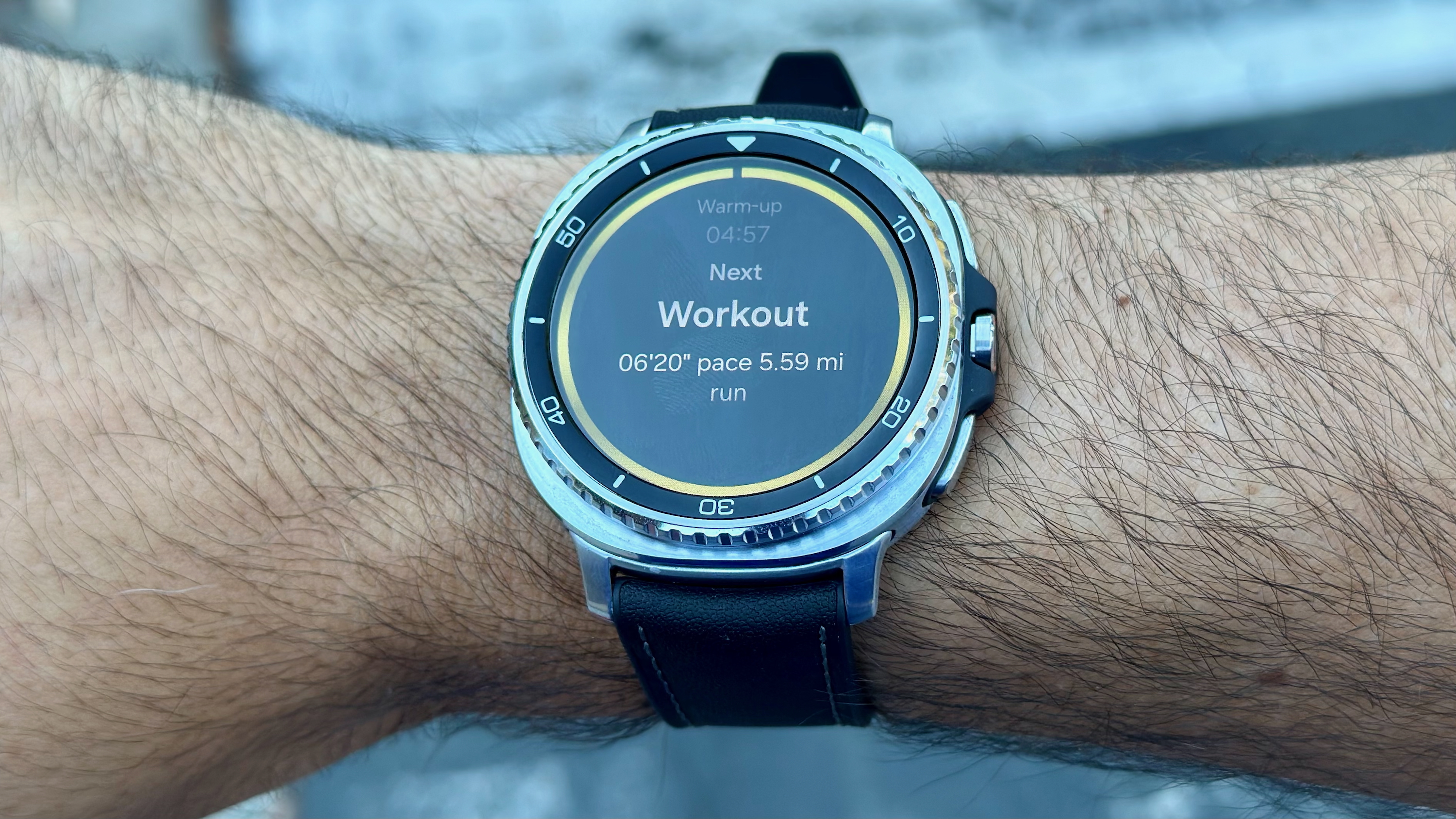 The Samsung Galaxy Watch 8 Classic on a wrist showing the next Workout step for Running Coach with pace and mileage.