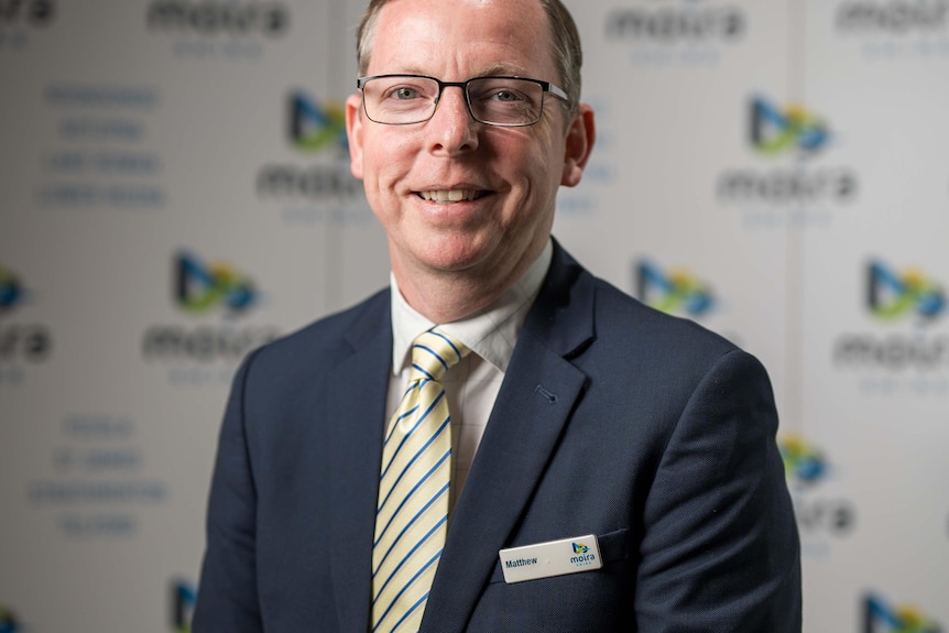 A man wearing a blue suit and a striped tie with short hair and glasses